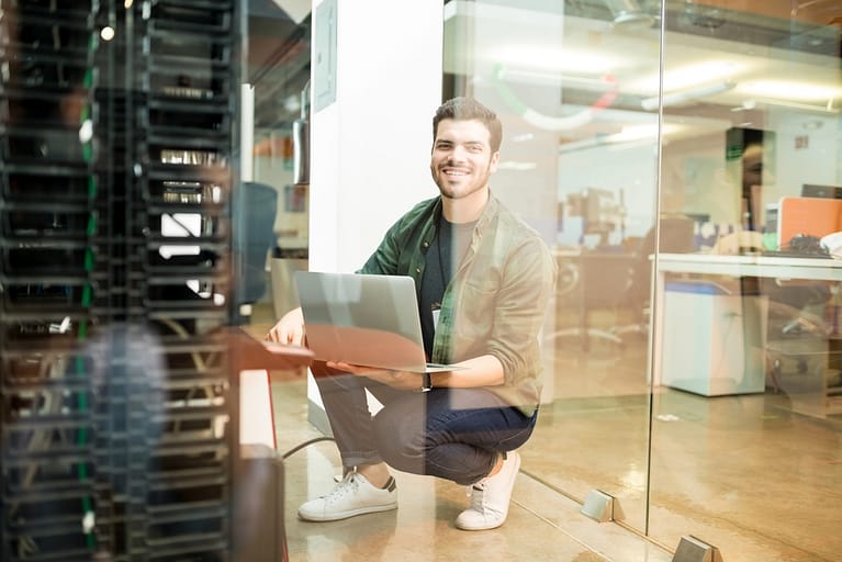 portrait-happy-young-male-network-engineer-with-laptop-hand-working-datacenter-1-scaled.jpg